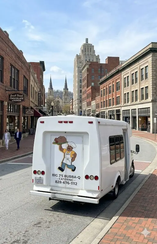 Big J’s Bubba-Q white catering shuttle parked on a city street in downtown Asheville North Carolina with historic brick buildings and a church in the background.